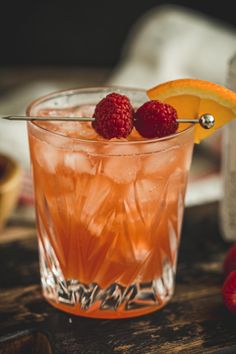 a close up of a drink with raspberries on the rim and an orange slice