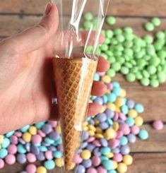 a hand holding an ice cream cone with candy candies in the background