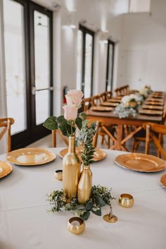 the table is set with gold vases and flowers