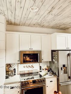 a kitchen with white cabinets and silver appliances in the center is decorated with wood planks on the ceiling