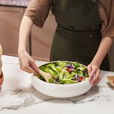 a woman in an apron is preparing a salad