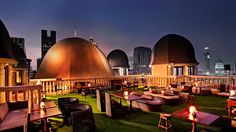 an outdoor seating area with tables and chairs on the grass in front of city skyline