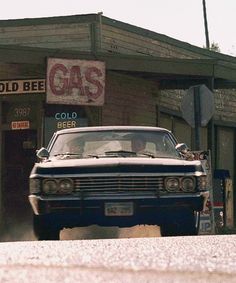 an old car is parked in front of a gas station