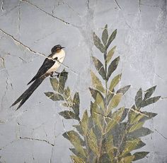 a bird sitting on top of a leafy branch next to a wall mural with leaves