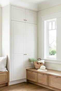 an empty room with white cupboards and wooden bench in front of a large window