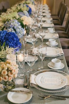 a long table is set with white and blue plates, silverware, and flowers