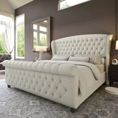 a large white bed sitting inside of a bedroom next to a window with curtains on the windowsill