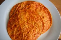 three tortillas on a white plate with a wooden table in the back ground