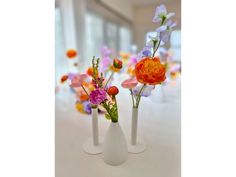 three white vases with different colored flowers in them on a table next to each other