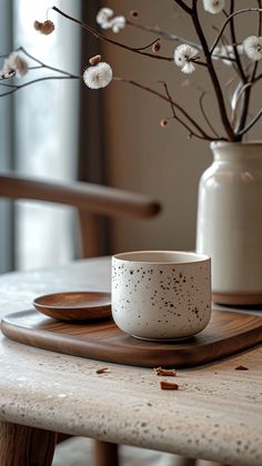 a white cup sitting on top of a wooden table next to a vase filled with flowers