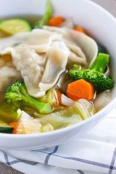 a white bowl filled with dumplings and vegetables on top of a blue and white towel