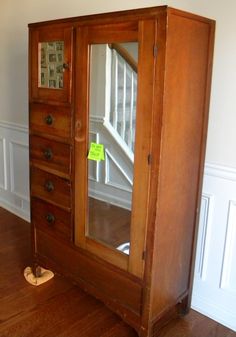 an old wooden armoire with a mirror on the front and bottom doors, in a room with hard wood floors