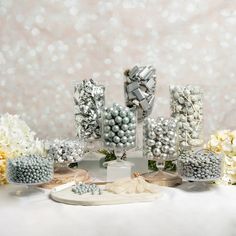 a table topped with lots of white and blue candies next to vases filled with flowers