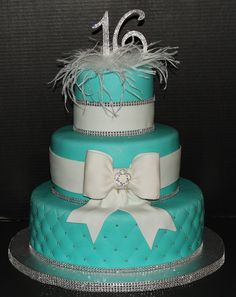 a three tiered cake decorated with white and blue ribbon, bow, and diamond decorations