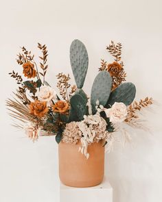 a vase filled with flowers and greenery on top of a white pedestal against a wall