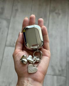 a hand holding a silver cell phone with a heart charm on it's keychain