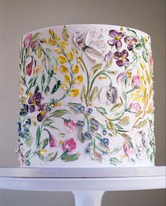 a white cake decorated with flowers and leaves on top of a stand in front of a wall