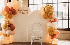 an arch made out of balloons with the words here comes the sun on it