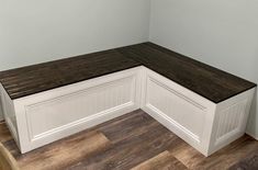 a corner bench in the corner of a room with wood flooring and white walls