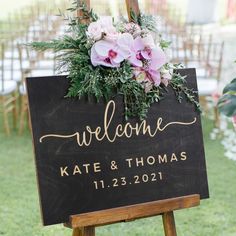 a welcome sign with flowers and greenery is displayed on a wooden easel in the grass