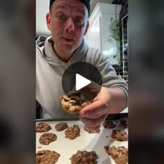 a man holding up a doughnut in front of some cookies on a baking sheet