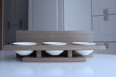 three white bowls are sitting on a wooden stand in the middle of a kitchen counter