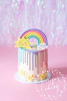 a cake with rainbow icing and stars on the top is sitting in front of a pink background