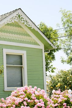 a green house with pink flowers in the front yard