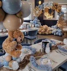 a teddy bear sitting on top of a table with balloons in the shape of animals