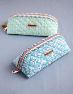 two small zippered purses sitting next to each other on a blue surface with white flowers