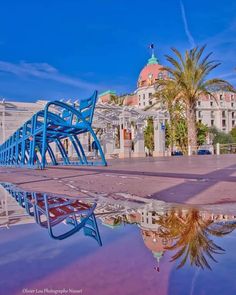 a blue bench sitting on top of a puddle in front of a tall white building