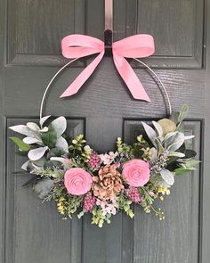 a wreath with pink flowers and greenery hanging on a door