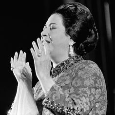 a woman with her hands in the air while singing into a microphone and wearing an elaborate dress