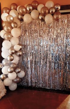 balloons and streamers are hanging from the wall in front of a mirror backdrop that is draped with silver sequins