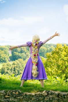 a woman in a purple dress standing on top of a lush green field with her arms outstretched