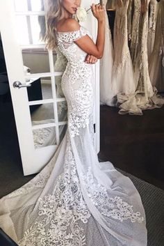 a woman standing in front of a mirror wearing a wedding dress with white lace on it