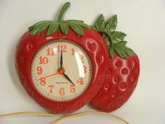 a red clock with two strawberries attached to it's sides on a white wall