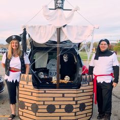 two people dressed up in costumes standing next to a pirate ship with skulls and bones on it