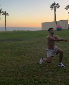 a shirtless man playing frisbee on the grass near palm trees at sunset