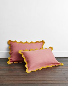 two pink and yellow pillows sitting on top of a wooden floor next to a white wall