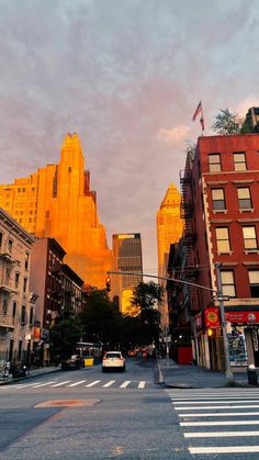 a city street with cars and buildings in the background at sunset or sunrise, as seen from across the street