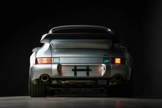 the back end of a silver sports car in a dark room with its lights on