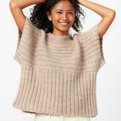 a woman with curly hair is smiling and wearing a tan knit sweater over her shoulders