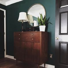 a dark green painted room with a wooden dresser and mirror on the wall next to it