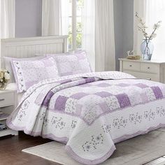 a bed with purple and white bedspread in a bedroom next to a window