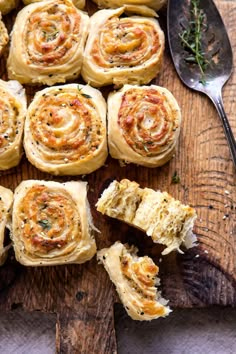 a wooden cutting board topped with rolls covered in different toppings next to a spoon