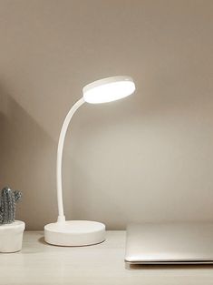 a white desk lamp sitting on top of a table next to a laptop and cactus