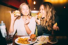 two women eating hamburgers and fries at a restaurant