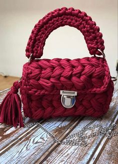 a red handbag sitting on top of a wooden table next to a metal chain