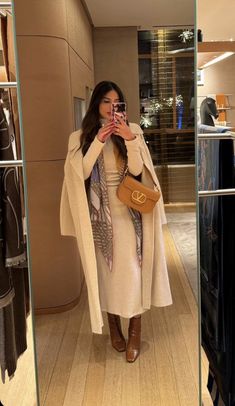 a woman taking a selfie in front of a mirror wearing a coat and scarf